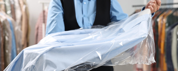 dry cleaning professional holds out a blue shirt wrapped in plastic