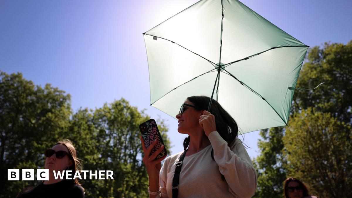 Two women wearing sunglasses on a sunny day. One carrying an umbrella and mobile phone