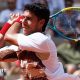 Adolfo Daniel Vallejo, wearing a white patterned t-shirt, plays a backhand with his yellow, blue and black racquet held in two hands over his right shoulder