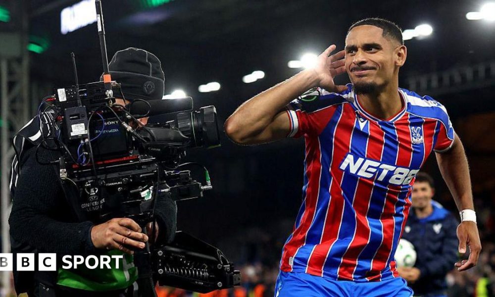 Crystal Palace's Maxence Lacroix cups his right ear with his right hand as he stands next to a TV camera
