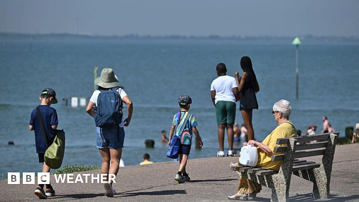 A beach prominade with one lady sitting on a bench while others are walking and looking out to sea
