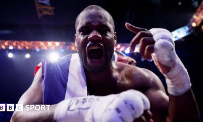 Daniel Dubois leans over the ropes of a boxing ring and holds up his hand