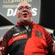 Stephen Bunting celebrates, pointing with both index fingers and pulling a celebratory facial pose as he wears a black and red darts shirt