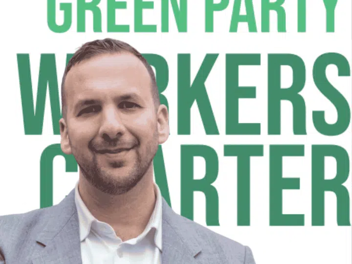 Zack Polanski smiling in front of the new Worker's Charter leaflet