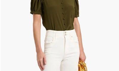 A woman wearing a short-sleeve olive top with off-white pants, and carrying a gold handbag in one hand
