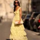 Emilie Joseph @in_fashionwetrust wears black sunglasses, a pale yellow with green and yellow flower print pattern V-neck / tank-top / backless / belted / ruffled maxi long dress, a beige fabric ruffled clutch, silver rings, pale yellow matte leather pointed pumps heels shoes, during a street style fashion photo session, on March 26, 2022 in Paris, France.