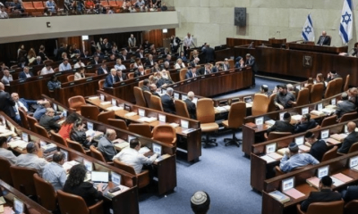A view of the Knesset in Israel with people sat on the pew-type chairs inside with only the backs of their bodies visible