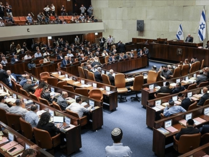 A view of the Knesset in Israel with people sat on the pew-type chairs inside with only the backs of their bodies visible