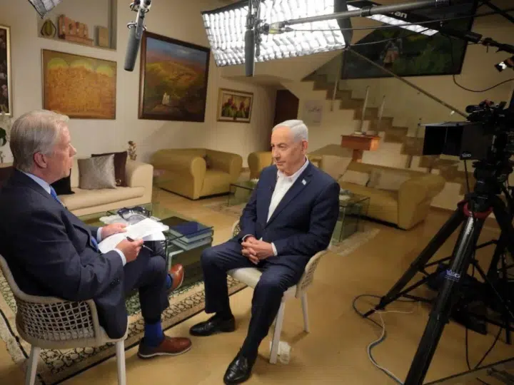 Israeli Prime Minister Benjamin Netanyahu sits across from CBS News reporter Major Garrett in a living room setting with the standing lights shining on them