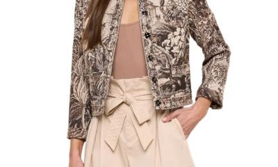 A woman wearing a tapestry blazer, light brown top, and cream-colored shorts with a bow