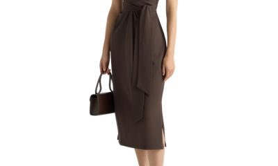 A woman wearing a brown dress and brown flats and carrying a hand bag