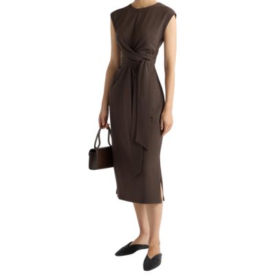 A woman wearing a brown dress and brown flats and carrying a hand bag