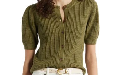 A woman wearing an olive green cardigan, white pants, and a cream-colored belt