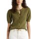 A woman wearing an olive green cardigan, white pants, and a cream-colored belt
