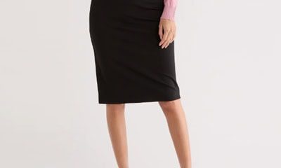 A woman wearing a white top, pink cardigan, black skirt, and white kitten heels