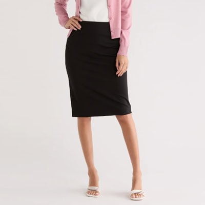 A woman wearing a white top, pink cardigan, black skirt, and white kitten heels
