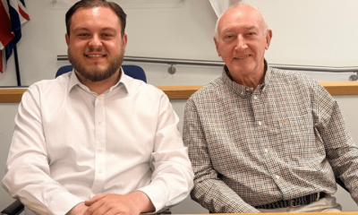 Sam Journet, wearing a white shirt with the top button undone, sat at a table smiling next to his Reform UK Basildon deputy leader, Jeff Noble. Journet is leader and an Essex County Council cabinet member