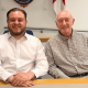 Sam Journet, wearing a white shirt with the top button undone, sat at a table smiling next to his Reform UK Basildon deputy leader, Jeff Noble. Journet is leader and an Essex County Council cabinet member
