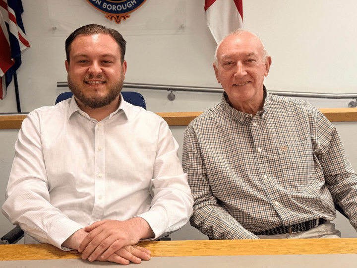 Sam Journet, wearing a white shirt with the top button undone, sat at a table smiling next to his Reform UK Basildon deputy leader, Jeff Noble. Journet is leader and an Essex County Council cabinet member