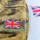 Close up of a soldier's arm in camo with a union flag badge. A union flag is flying in the background. Defence Universities Alliance