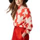 A woman wearing a woven wide-brim hat, red-orange pants, and red-orange/white floral blouse