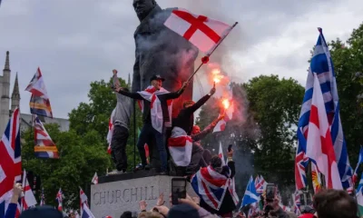 People, largely white men, sit on a Winston Churchill statue with flares and wearing Union Jack, England and Scotland flags as they take part in the rally where Muslims experienced hate speech