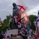 People, largely white men, sit on a Winston Churchill statue with flares and wearing Union Jack, England and Scotland flags as they take part in the rally where Muslims experienced hate speech