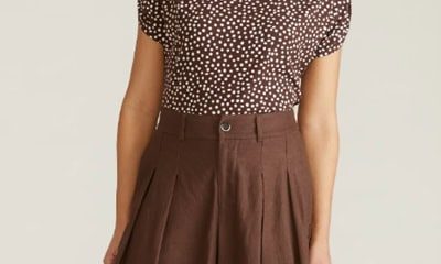 A woman (head and lower legs cropped out) wearing brown wide-leg pants and a brown-and-white polka dot top
