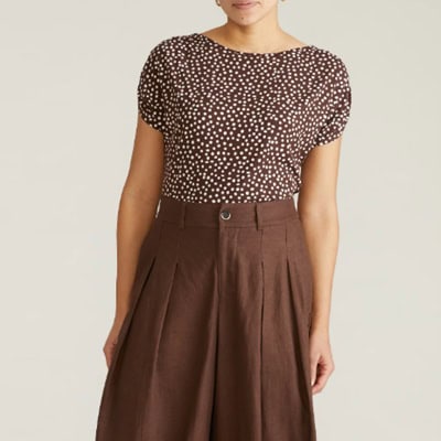 A woman (head and lower legs cropped out) wearing brown wide-leg pants and a brown-and-white polka dot top