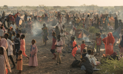 Adults and children stand and sit in the remote desert landscape of Sudan