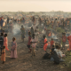 Adults and children stand and sit in the remote desert landscape of Sudan