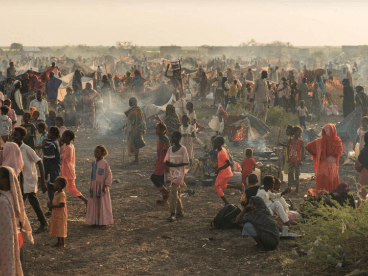 Adults and children stand and sit in the remote desert landscape of Sudan