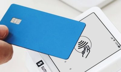 person holds blue credit card at a payment station (tap to pay)