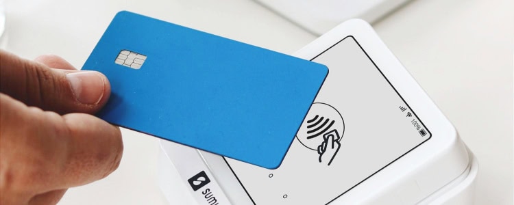 person holds blue credit card at a payment station (tap to pay)