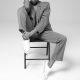 professional woman wears a suit and sneakers; she is sitting on a chair with one leg drawn up.