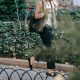 Black woman walks outside on her way to work; she is wearing what could be some of the best work pants for women in 2024! She's carrying a tote bag and drinking a coffee while she walks behind a short circular fence