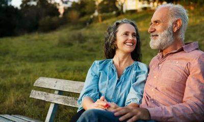 A couple sitting on a bench at sunset smiling at each other