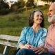 A couple sitting on a bench at sunset smiling at each other