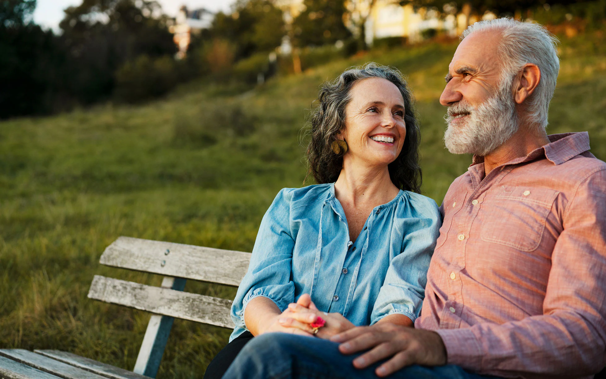 A couple sitting on a bench at sunset smiling at each other