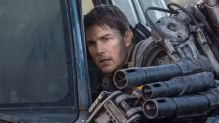 Tom Cruise as Cage wearing a mech-suit and hiding behind a car in Edge of Tomorrow