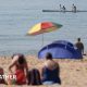 People on beach during May heatwave. One man wades in the sea whist two people paddle by in a kayak