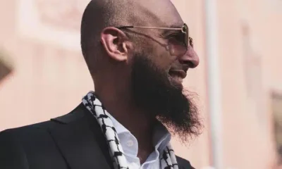 Majid Freeman, wearing sunglasses, smiles and looks into the distance. The stylish photograph captures his side profile.