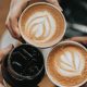 friends toast with lattes and another dark drink that is possibly soda or cold brew