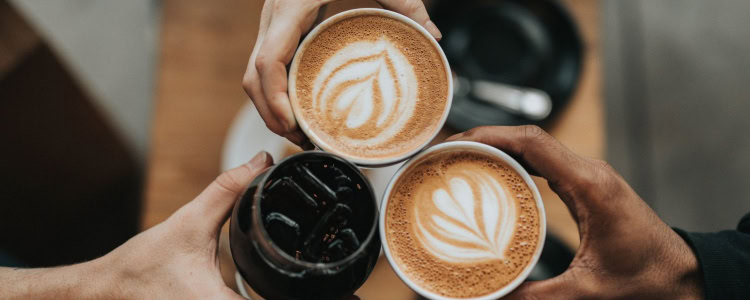 friends toast with lattes and another dark drink that is possibly soda or cold brew