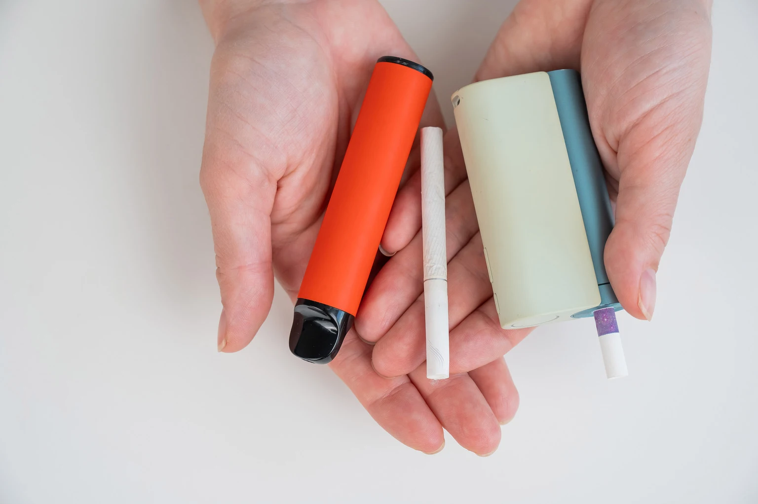 Woman holding regular, electronic cigarette and disposable vape on white background. Tobacco heating systems.