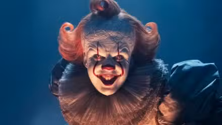 Bill Skarsgard as Pennywise bending over and smiling for the camera in It: Welcome to Derry.
