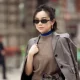 MILAN, ITALY - FEBRUARY 25: Willabelle Ong wears a cropped grey tailored blazer in smooth suiting fabric draped over the shoulders, layered over a taupe sleeveless knit top with a bright cobalt blue high-neck under layer, paired with a grey mini skirt in wool blend, accessorised with slim black rectangular sunglasses, gold hoop earrings and a wide brown leather belt with silver buckle, carrying a black leather clutch outside Jil Sander during the Milan Fashion Week - Womenswear Fall/Winter 2026/2027 on February 25, 2026 in Milan, Italy. (Photo by Raimonda Kulikauskiene/Getty Images)