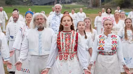 Pagan cult members hold their arms down and open during a ritual in Midsommar