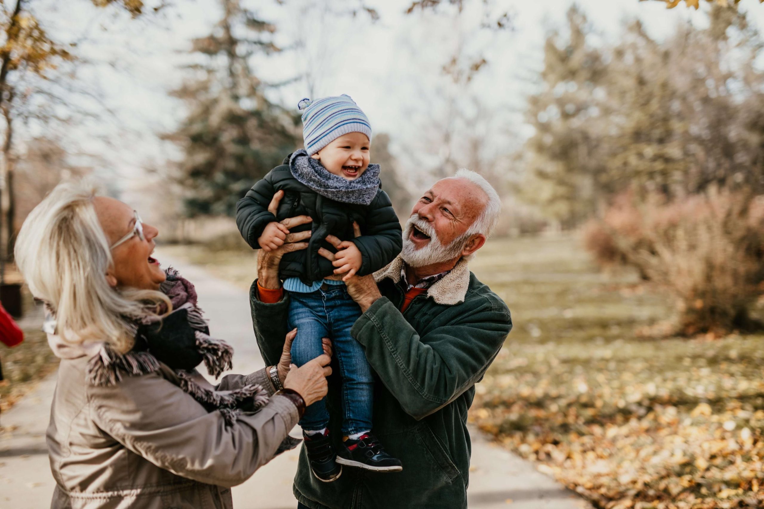 grandma and grandad lift small grandchild up in an embrace on a winter day