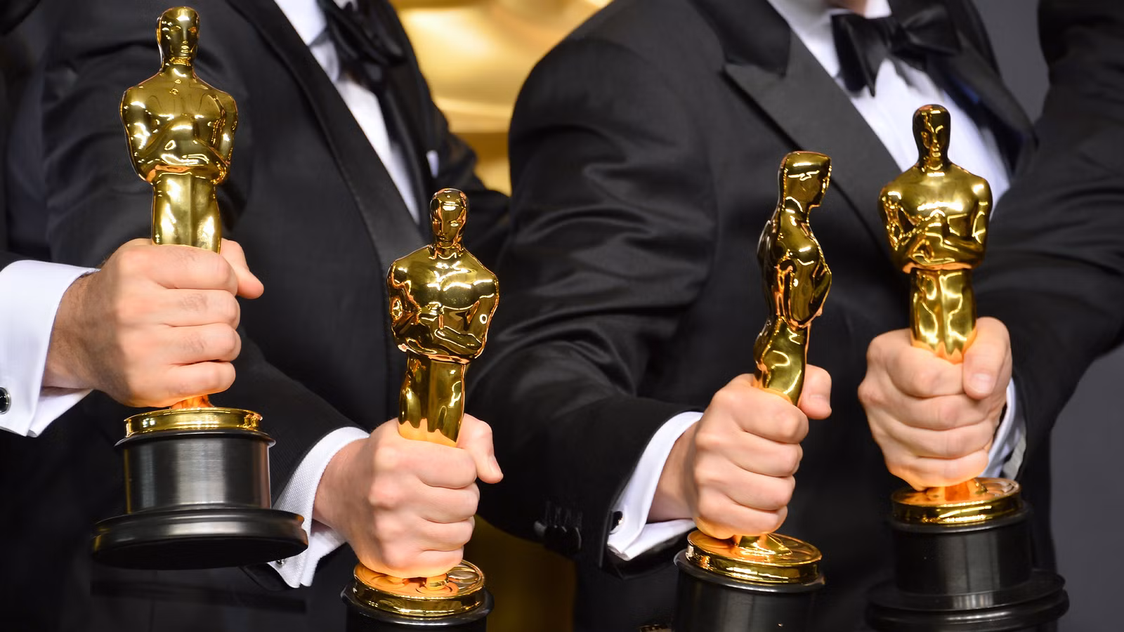 Four hands holding Oscar statues